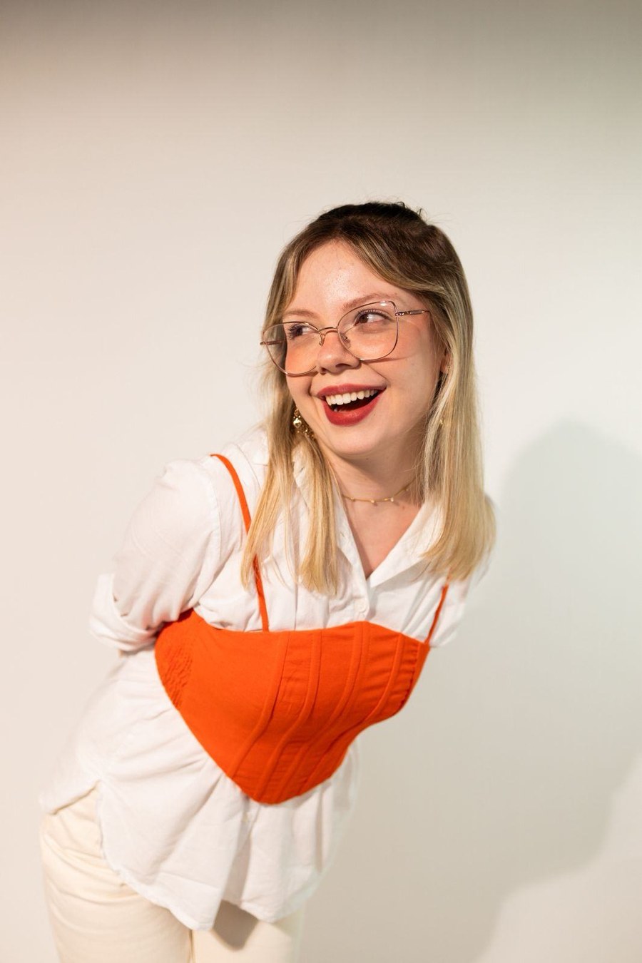 Laura Zanetti sorrindo, de camisa branca e corselet laranja